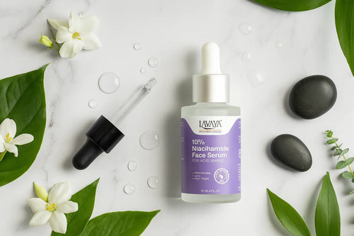  10% niacinamide face serum for acne marks with dropper bottle on white marble surface surrounded by white flowers and green leaves
